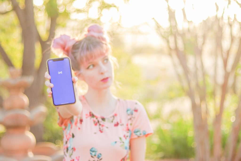 Woman in a floral dress holding up a phone that displays the Albert app