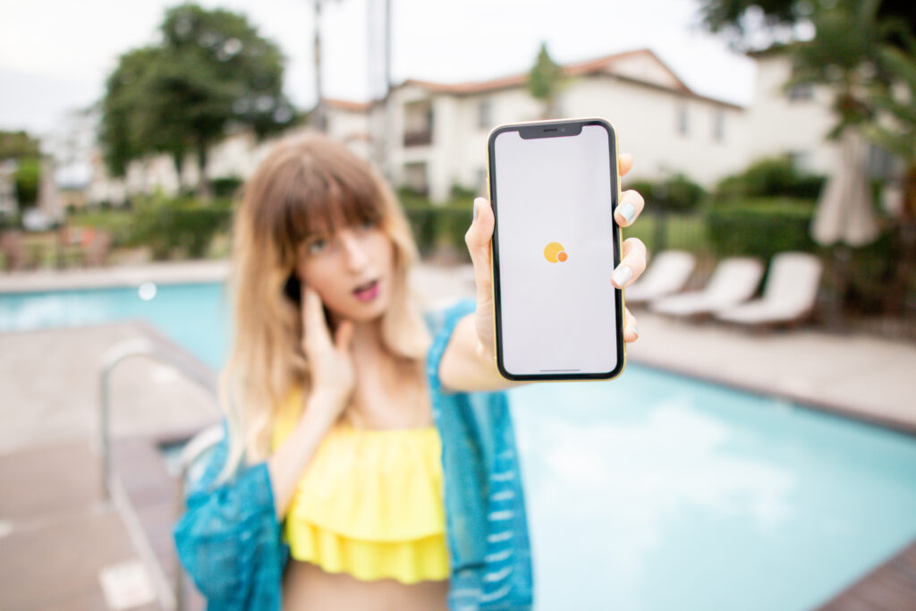 Woman standing by the pool, holding a phone that displays the Solo Funds app