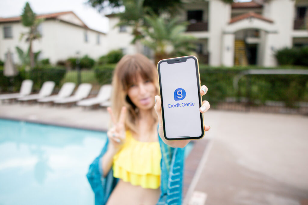 girl by the pool holding a phone that displays the credit genie app