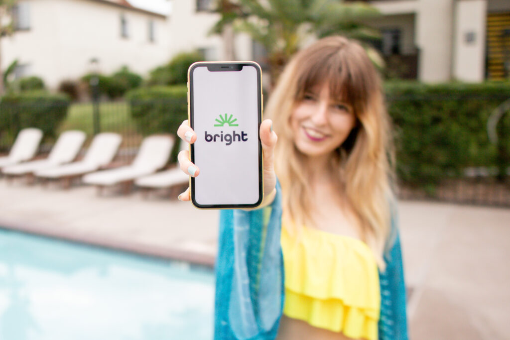 Smiling woman by the pool holding a phone that displays the bright money app