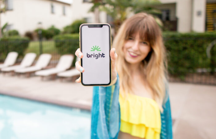 Smiling woman by the pool holding a phone that displays the bright money app