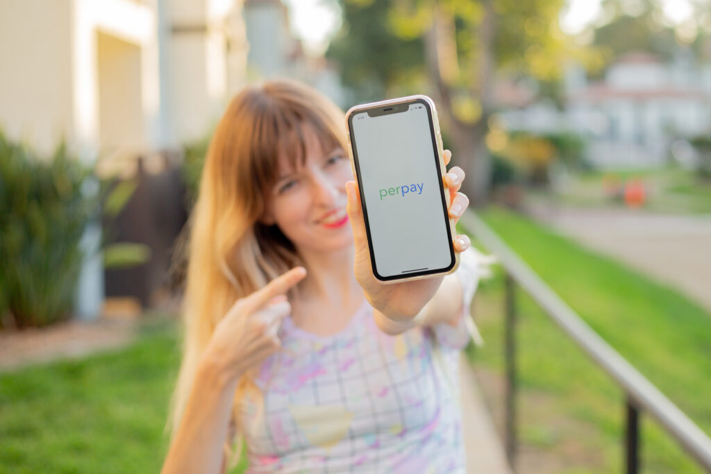 Smiling girl holding and pointing at a phone that displays the Perpay app